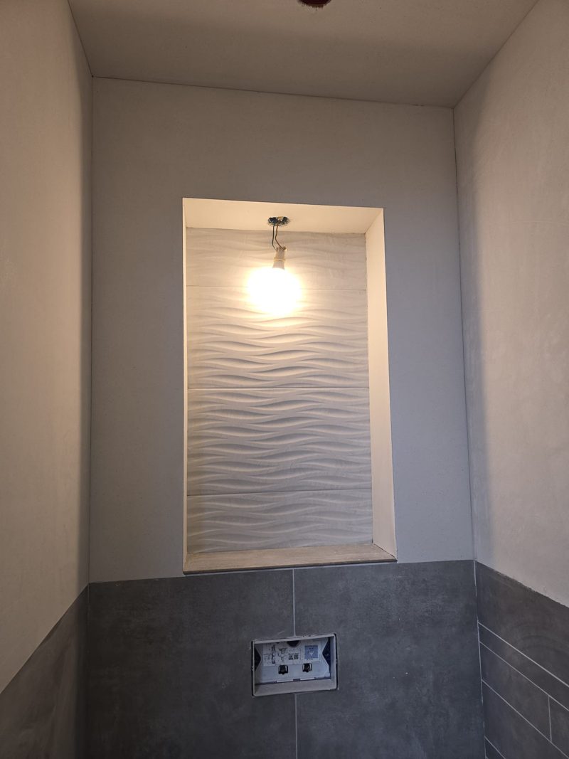 Toilet with plastered walls and ceiling above dark tiling, a niche with a lamp in the middle