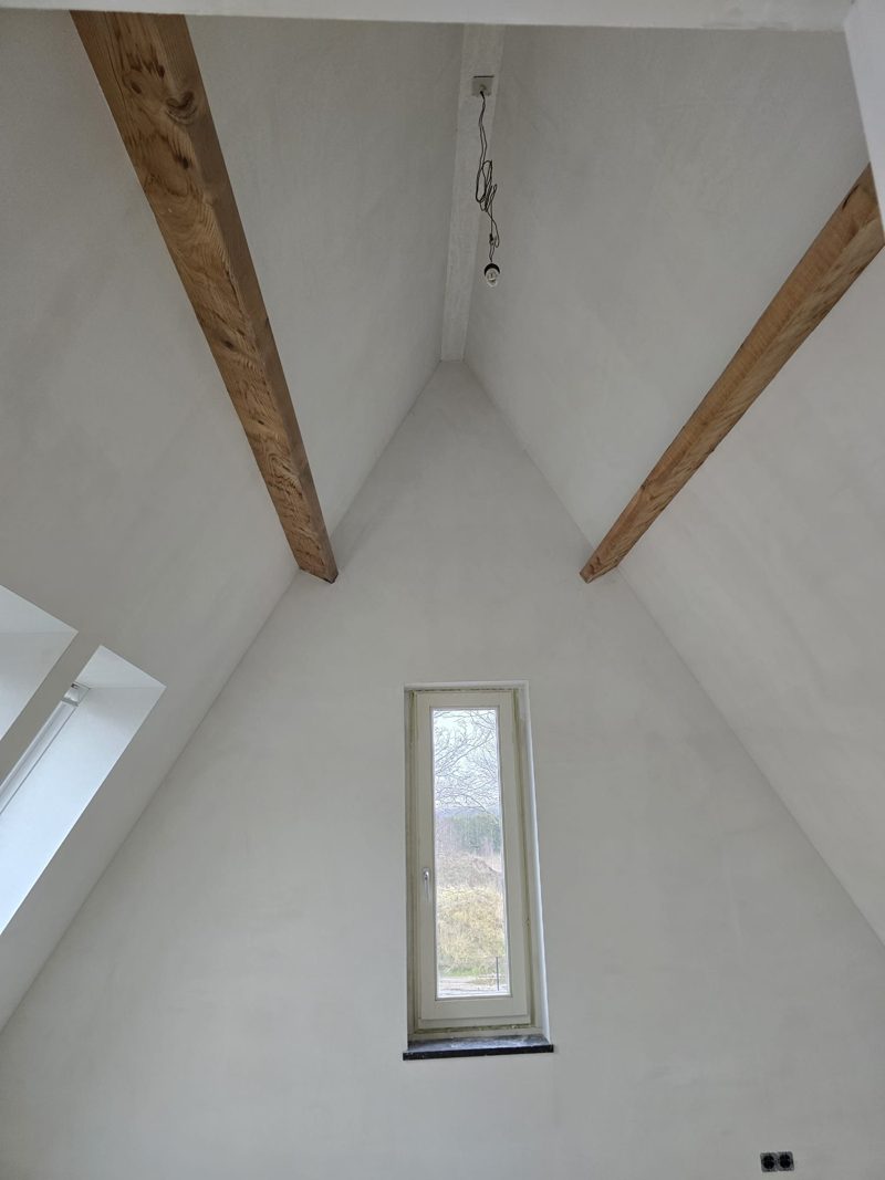 Attic seen from below: two timber roof trusses, sloping ceilings and the gable wall with a narrow window, all plastered smooth