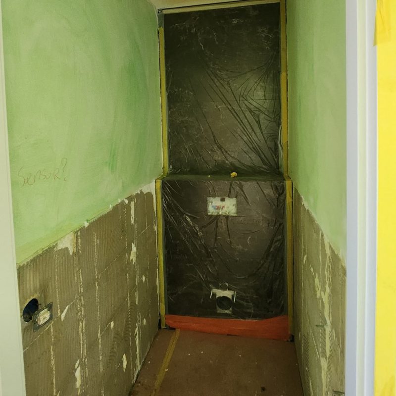 Voor: smal toilet met een groene laag op de wanden en een afgedekte inbouwwand