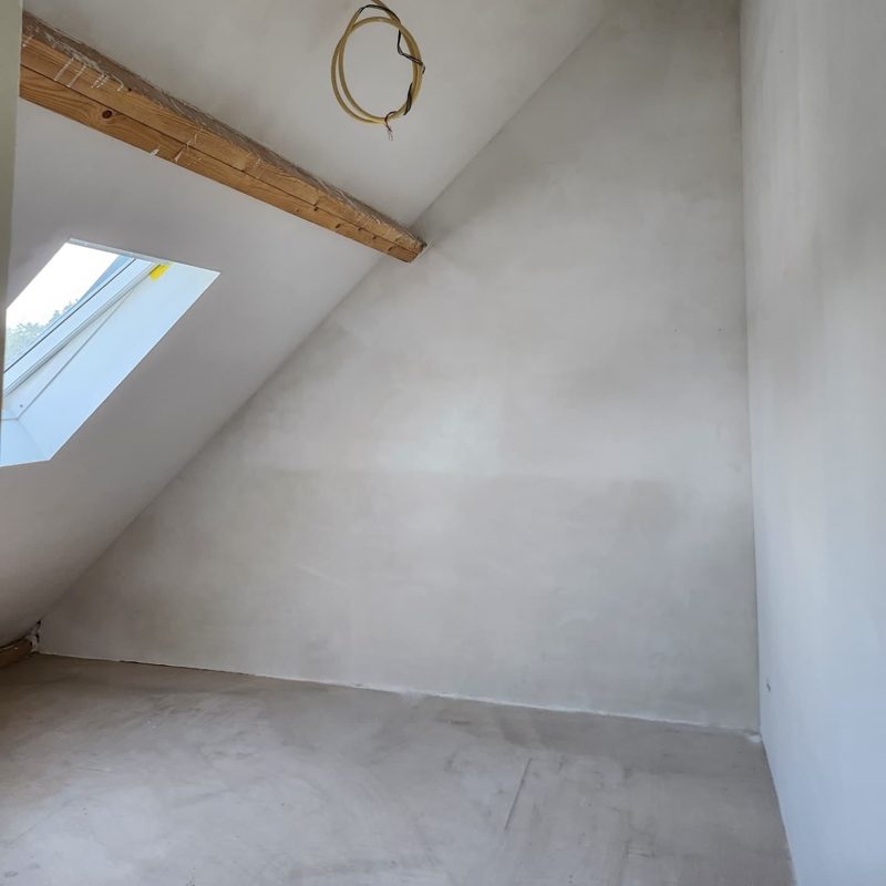 Zolderkamer met een dakraam en een houten balk, schuine kap en wand glad gestuct